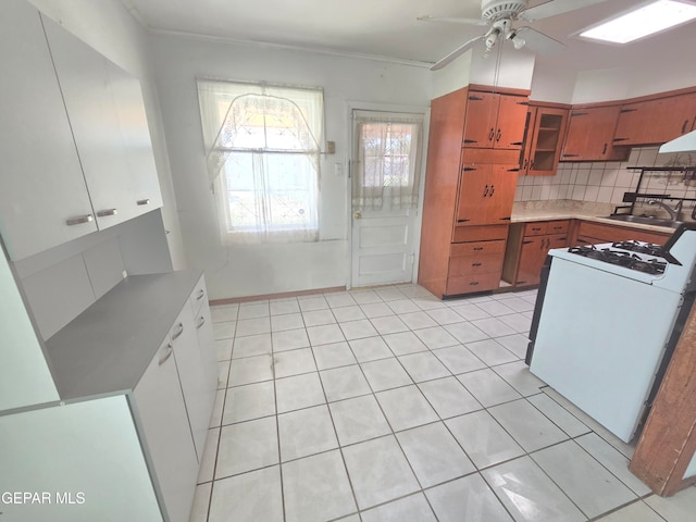 kitchen featuring decorative backsplash, white gas range oven, light tile patterned floors, ceiling fan, and sink