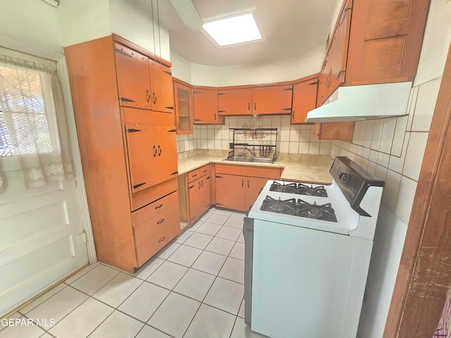 kitchen with decorative backsplash, sink, light tile patterned floors, and white gas range oven