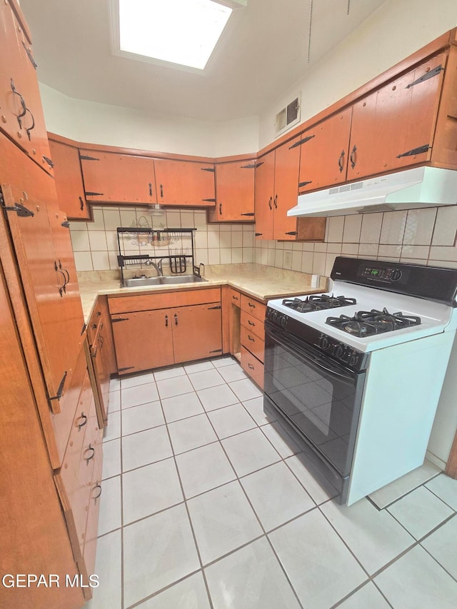 kitchen featuring white gas range, light tile patterned flooring, decorative backsplash, and sink