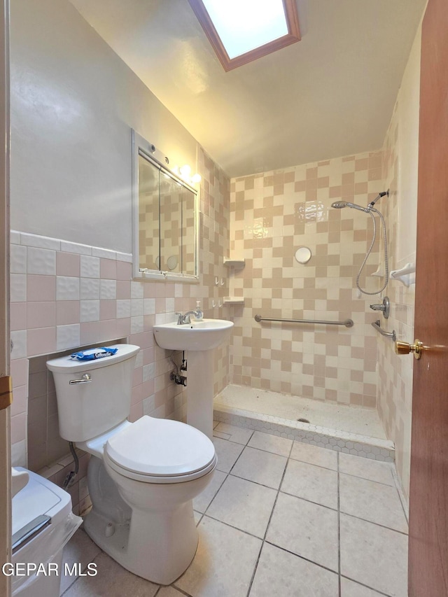 bathroom with a skylight, tiled shower, tile patterned floors, tile walls, and toilet