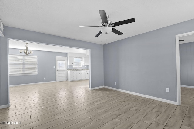 unfurnished living room with a textured ceiling, ceiling fan with notable chandelier, and light hardwood / wood-style floors