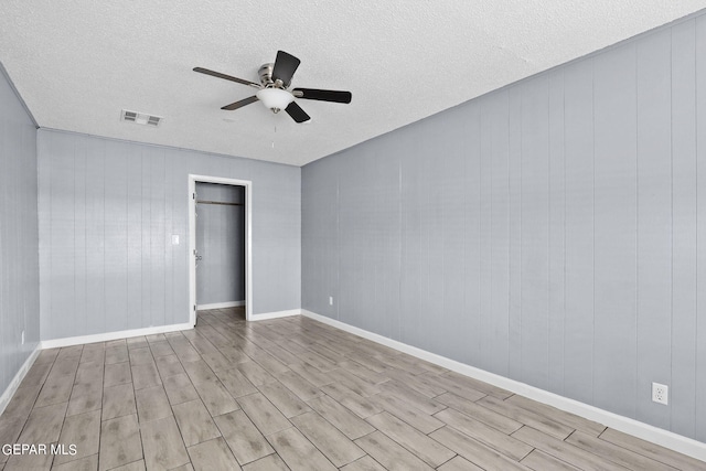 unfurnished room with light wood-type flooring, a textured ceiling, wooden walls, and ceiling fan