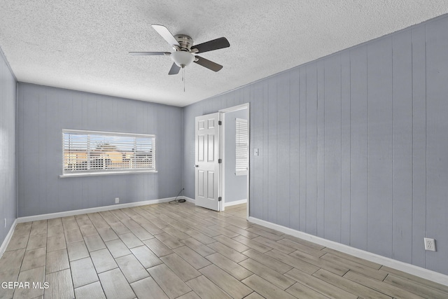 spare room with light hardwood / wood-style flooring, wooden walls, a textured ceiling, and ceiling fan