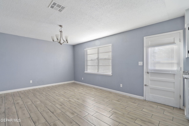 unfurnished room featuring a textured ceiling, a healthy amount of sunlight, light hardwood / wood-style flooring, and a chandelier