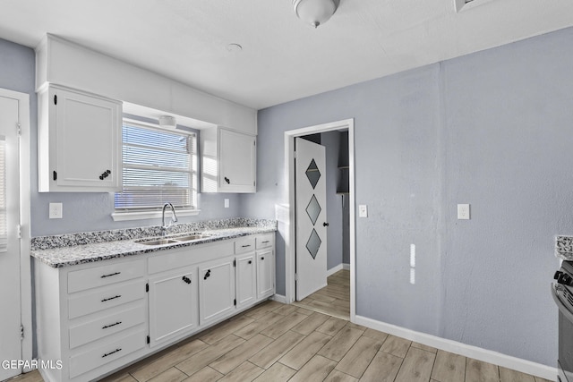 kitchen featuring light stone counters, light hardwood / wood-style floors, sink, white cabinets, and stainless steel range with electric stovetop