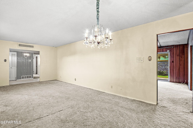 carpeted spare room with wooden walls, a textured ceiling, and an inviting chandelier