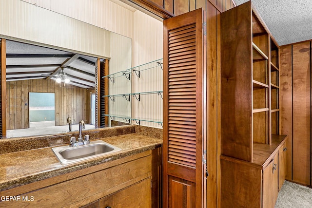 interior space with wood walls, sink, vaulted ceiling with beams, ceiling fan, and a textured ceiling