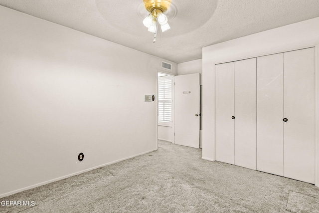 unfurnished bedroom featuring ceiling fan, a closet, light carpet, and a textured ceiling