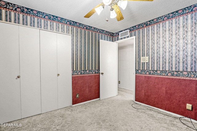 unfurnished bedroom with ceiling fan, light colored carpet, a textured ceiling, and a closet