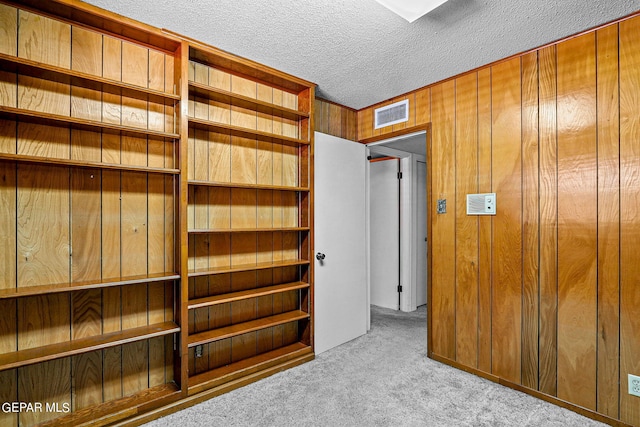 unfurnished bedroom with wood walls, light carpet, and a textured ceiling