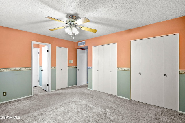 unfurnished bedroom with a textured ceiling, two closets, ceiling fan, and light colored carpet