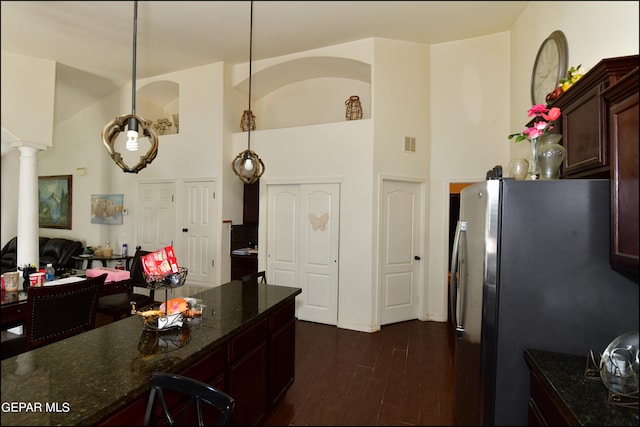 kitchen featuring stainless steel fridge, dark wood-type flooring, pendant lighting, ornate columns, and dark stone counters