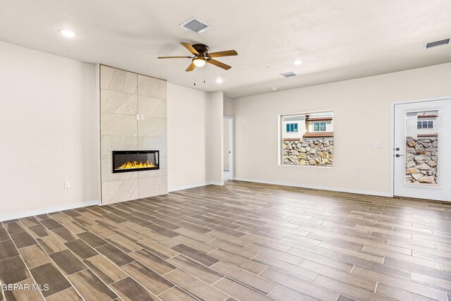 unfurnished living room featuring ceiling fan, dark wood-type flooring, and a tile fireplace