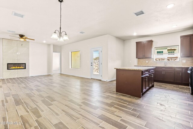 kitchen featuring pendant lighting, wood-type flooring, a center island, light stone countertops, and decorative backsplash