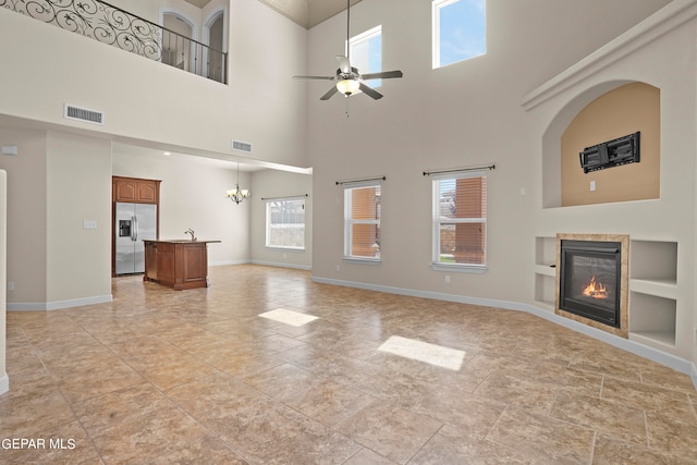 unfurnished living room with ceiling fan with notable chandelier, a high ceiling, and built in features