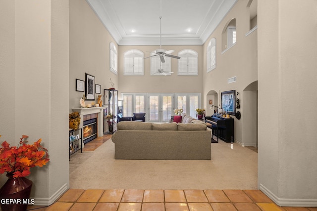 living room featuring a tiled fireplace, tile patterned floors, ornamental molding, a high ceiling, and ceiling fan