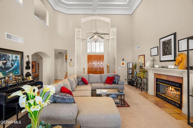 851 Via Alegre Ln, El Paso, TX 79912 - carpeted living room with a high ceiling, arched walkways, a tiled fireplace, ceiling fan, and crown molding
