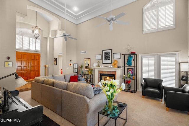 living room featuring ceiling fan, light colored carpet, a tiled fireplace, and a high ceiling