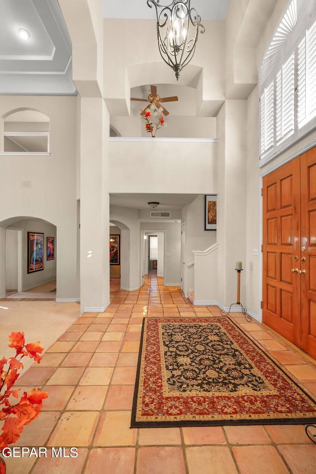 foyer entrance with ceiling fan with notable chandelier and a towering ceiling