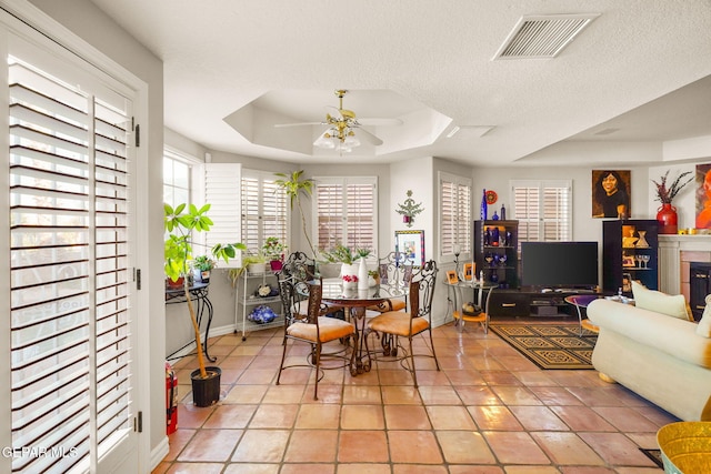 dining area with tile patterned flooring, ceiling fan, a raised ceiling, and a textured ceiling