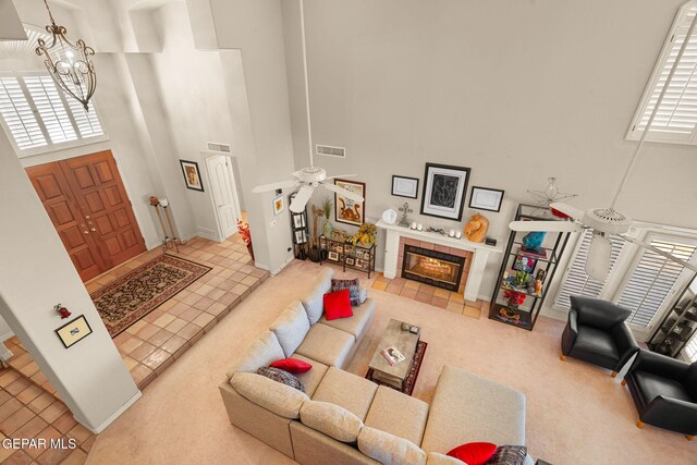 851 Via Alegre Ln, El Paso, TX 79912 - carpeted living room with a high ceiling, a chandelier, a tile fireplace, ceiling fan, and tile patterned floors