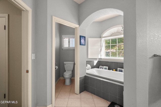 bathroom with tiled tub, toilet, and tile patterned floors