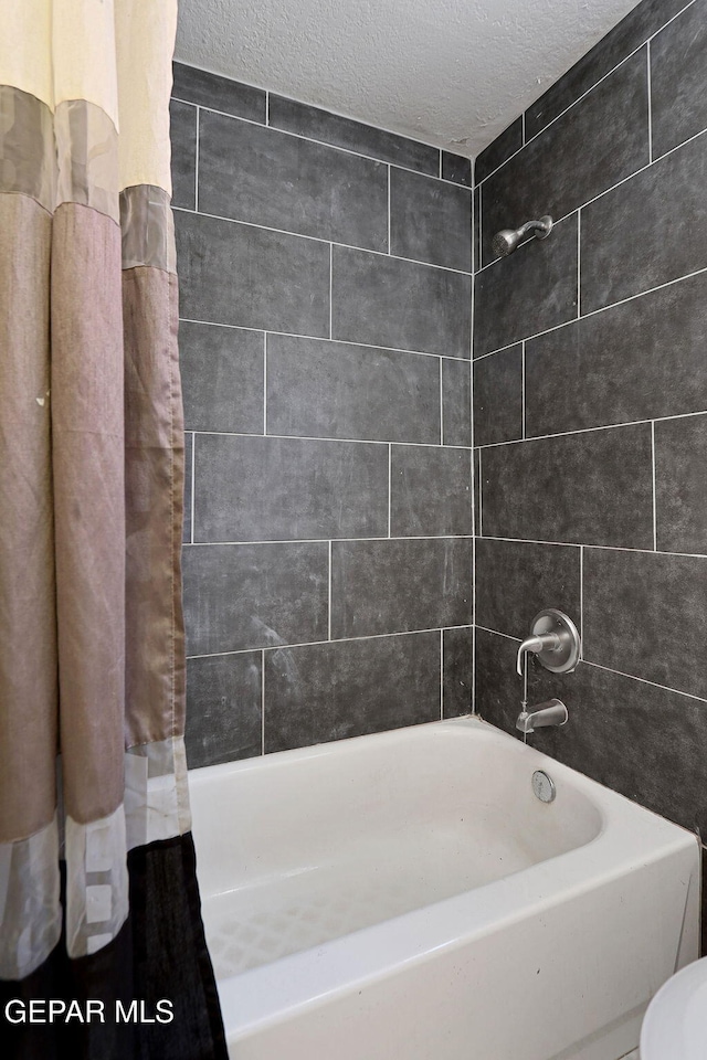 bathroom featuring toilet, shower / bath combination with curtain, and a textured ceiling