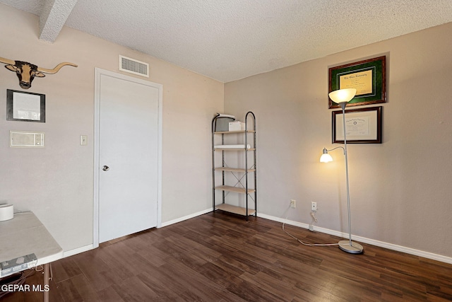 spare room featuring dark hardwood / wood-style flooring, a textured ceiling, and beam ceiling