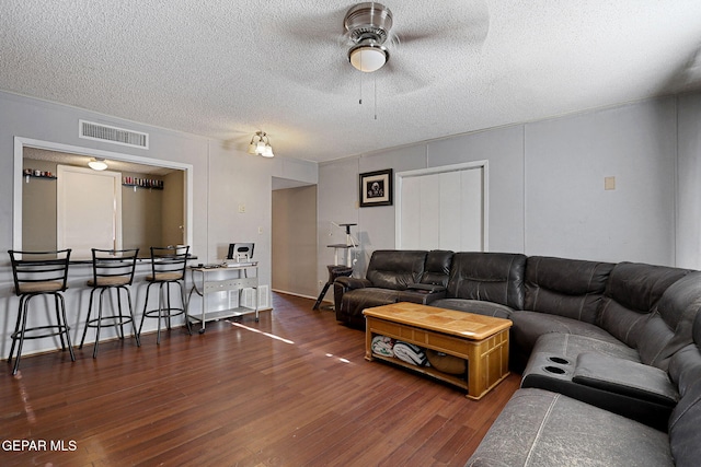 living room with dark wood-type flooring, a textured ceiling, and ceiling fan