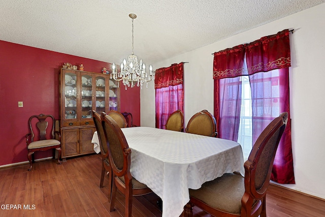 dining area featuring wood-type flooring, a notable chandelier, and a textured ceiling