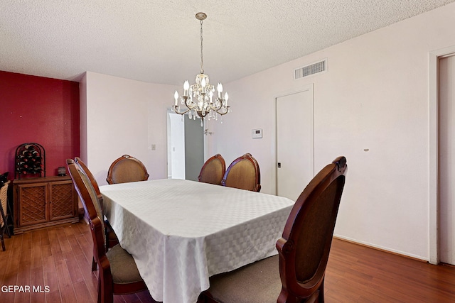 dining space with a textured ceiling, dark wood-type flooring, and a chandelier