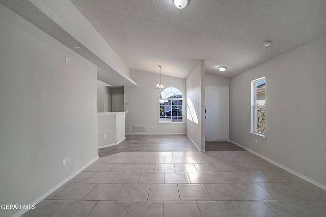 tiled entrance foyer with a textured ceiling, lofted ceiling, and a chandelier