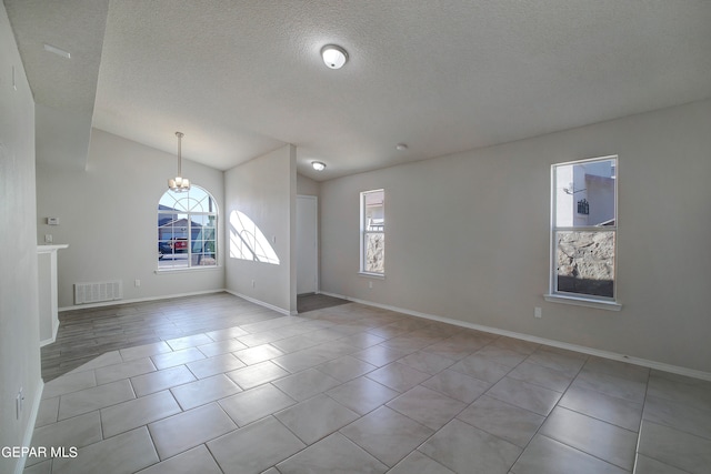 tiled spare room featuring a chandelier and a textured ceiling