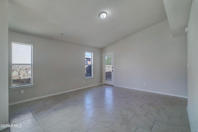 spare room with a textured ceiling, lofted ceiling, and light tile patterned floors