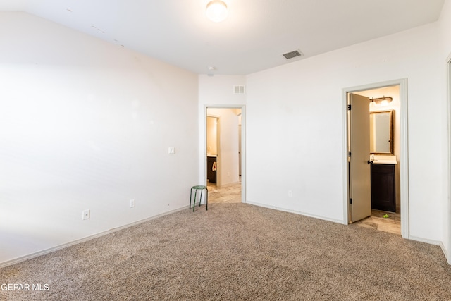 unfurnished bedroom featuring light carpet, connected bathroom, and vaulted ceiling