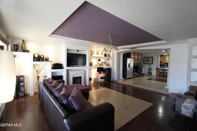 tiled living room with a tray ceiling, decorative columns, and built in features