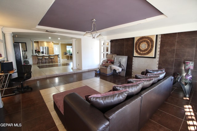 living room featuring tile walls, tile patterned flooring, a tray ceiling, and ornate columns