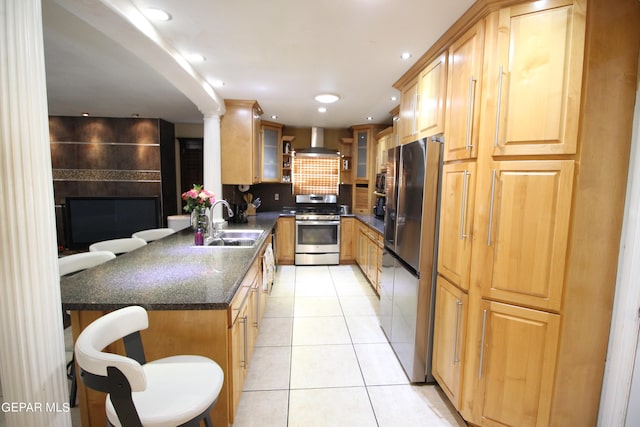 kitchen featuring sink, a kitchen bar, wall chimney exhaust hood, appliances with stainless steel finishes, and dark stone countertops