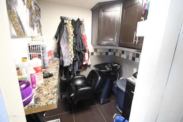 kitchen with dark brown cabinetry, decorative backsplash, dark tile patterned flooring, and light stone counters