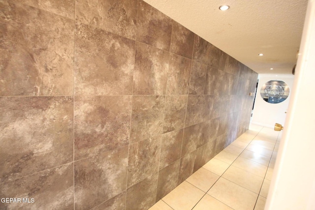 hallway featuring tile walls, tile patterned flooring, and a textured ceiling