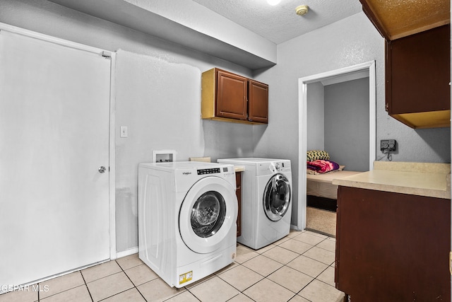 washroom featuring a textured ceiling, washer and clothes dryer, light tile patterned floors, and cabinets