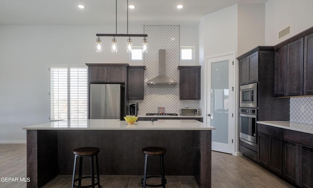 kitchen with wall chimney exhaust hood, plenty of natural light, appliances with stainless steel finishes, a center island, and light hardwood / wood-style floors