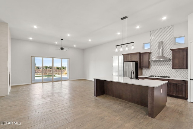 kitchen with light hardwood / wood-style flooring, a center island with sink, appliances with stainless steel finishes, and wall chimney range hood