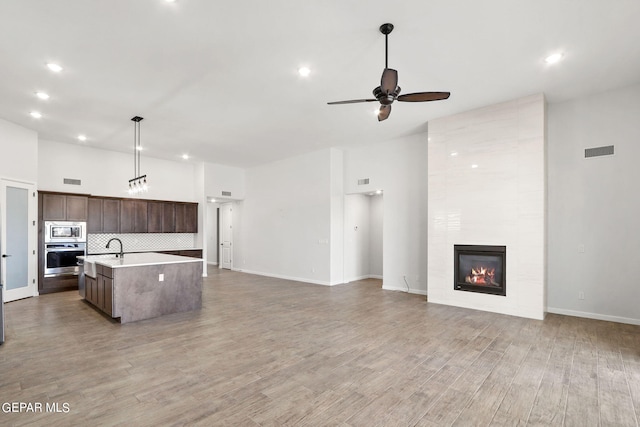 kitchen featuring stainless steel appliances, dark brown cabinetry, a large fireplace, a center island with sink, and hardwood / wood-style floors