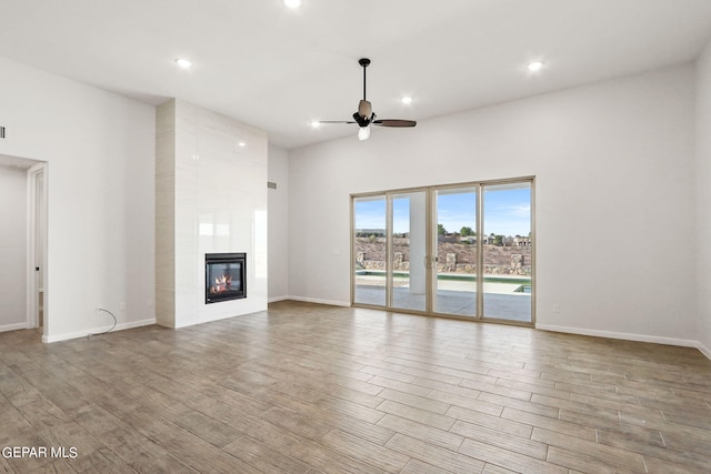 unfurnished living room with a high ceiling, light hardwood / wood-style floors, a fireplace, and ceiling fan