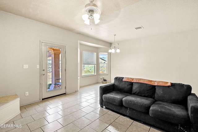 living room featuring ceiling fan with notable chandelier, a textured ceiling, and light tile patterned floors