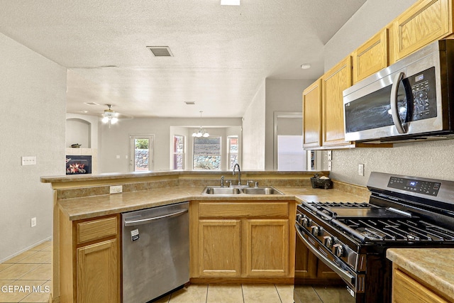 kitchen with a textured ceiling, sink, a tiled fireplace, kitchen peninsula, and appliances with stainless steel finishes