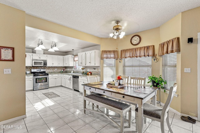 kitchen with white cabinetry, stainless steel appliances, hanging light fixtures, light tile patterned floors, and a textured ceiling