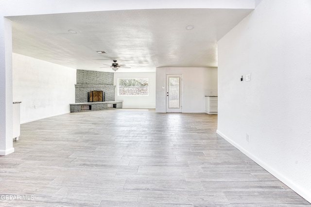 unfurnished living room featuring a brick fireplace, light hardwood / wood-style flooring, and ceiling fan