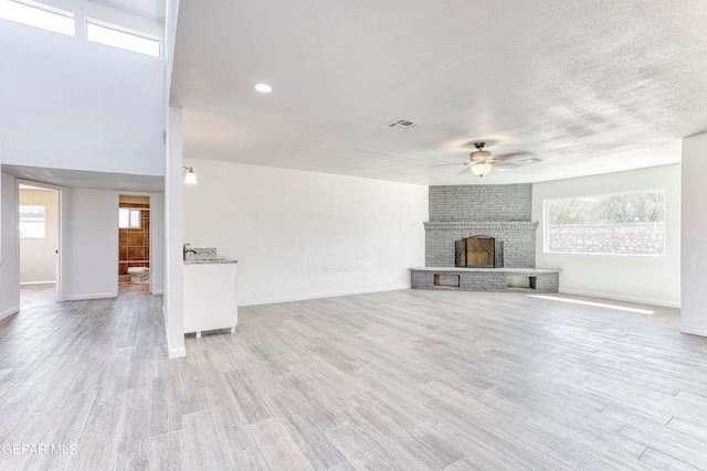 unfurnished living room with a brick fireplace, light wood-type flooring, and ceiling fan